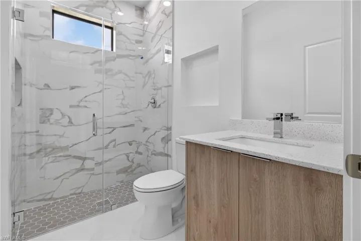 Spacious bathroom featuring a glass-enclosed shower with large format tile and hexagonal floor tile, a natural wood-finish vanity with an integrated sink and light-colored countertop, and recessed lighting