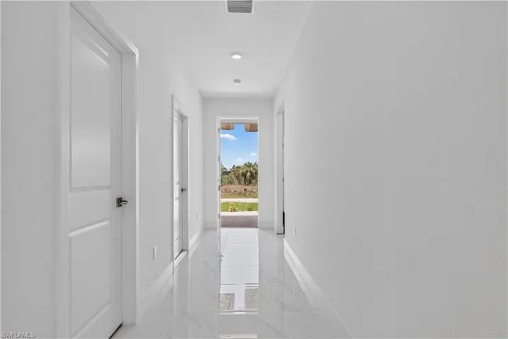 Bright hallway featuring recessed lighting, white walls, white doors with dark hardware, and glossy tile flooring