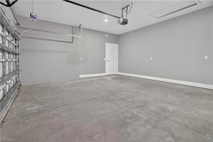Spacious garage featuring a concrete floor, light gray walls, white trim, and a white interior door