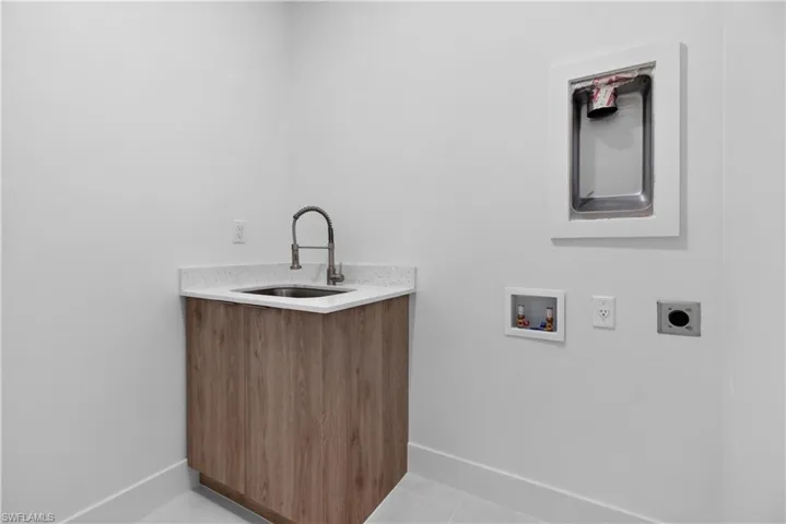 Utility room featuring a wood-finish cabinet with a sink, light-toned countertop, wall-mounted laundry hookups, and floor tiling