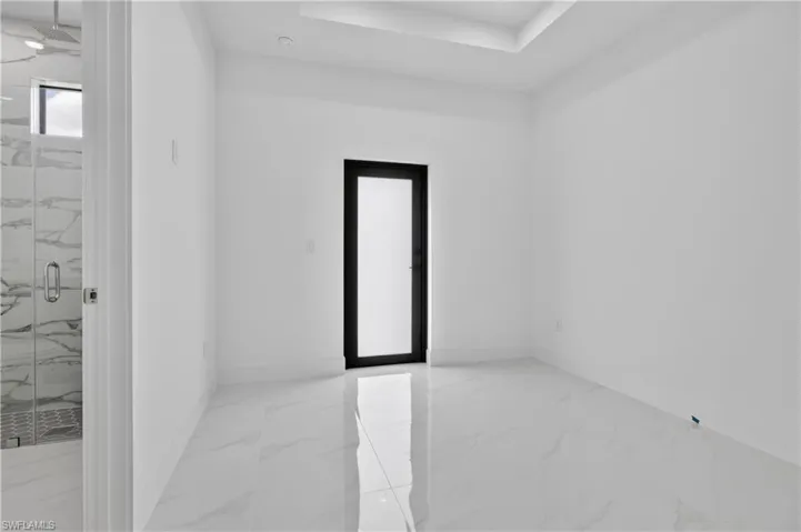Spacious interior room featuring large format tile flooring, a black-framed opaque door, and a recessed ceiling detail