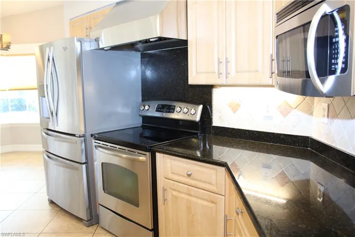 Kitchen featuring ventilation hood, appliances with stainless steel finishes, light brown cabinets, decorative backsplash, and light tile patterned flooring