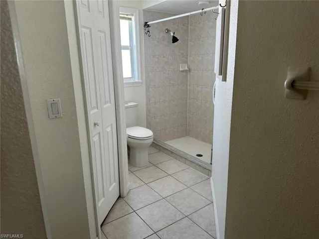 Bathroom with a textured wall, a stall shower, a closet, and light tile patterned floors