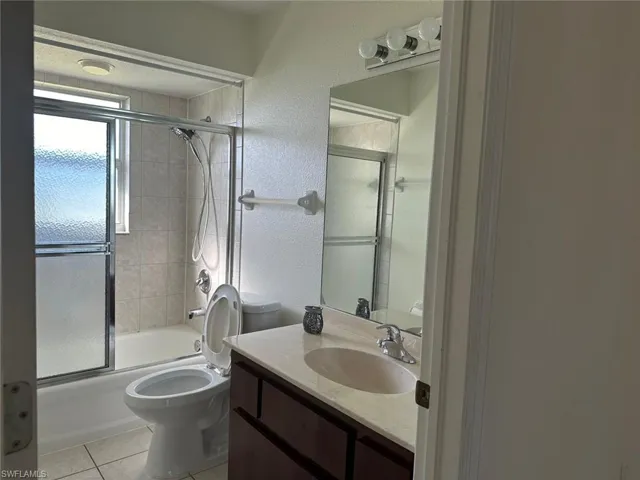 Bathroom featuring a textured wall, vanity, combined bath / shower with glass door, and light tile patterned floors