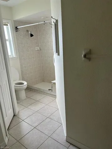 Full bathroom featuring a shower stall, light tile patterned floors, and a textured wall