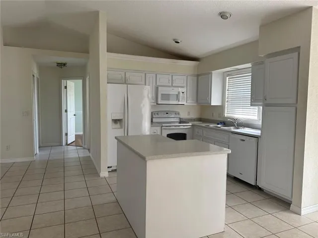 Kitchen with white appliances, light countertops, vaulted ceiling, light tile patterned floors, and a kitchen island