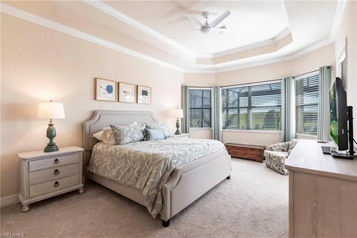 Bedroom with crown molding, bay window, ceiling fan, tray ceiling, and door to the lanai.
