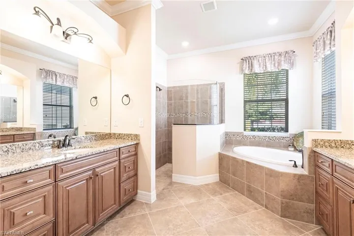 Bathroom featuring double vanities, walk-in shower with separate soak tub, and crown molding