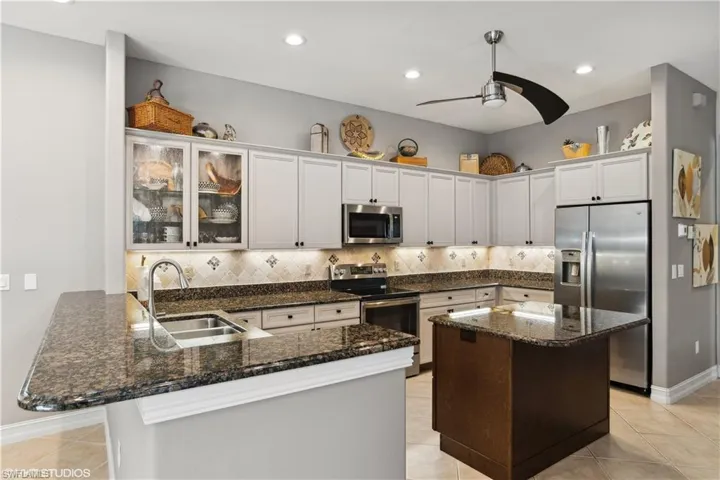 Kitchen with stainless steel appliances, dark stone countertops, backsplash, and light tile floors