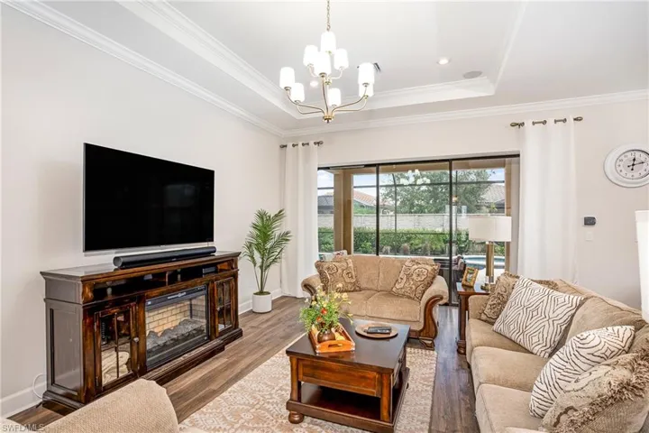 Living room featuring a raised ceiling, wood finished floors, ornamental molding, recessed lighting, and a chandelier
