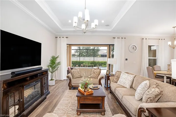 Living area with a chandelier, wood finished floors, crown molding, and a raised ceiling