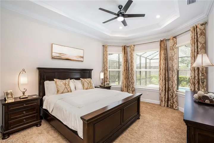 Bedroom featuring multiple windows, ornamental molding, a raised ceiling, light colored carpet, and ceiling fan