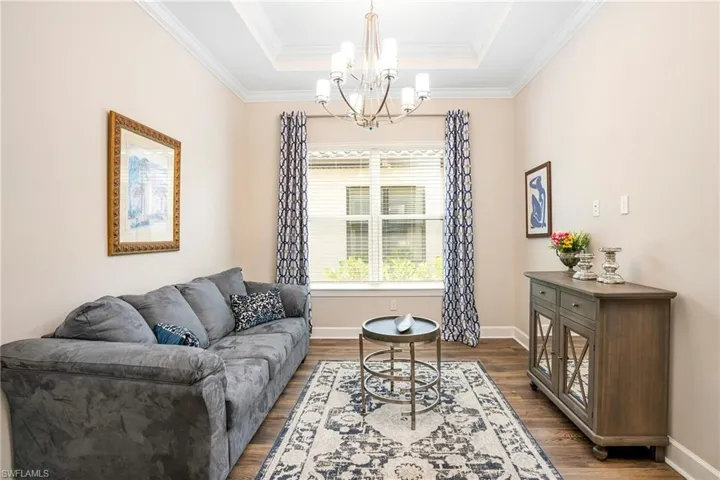 Living room with dark wood-style flooring, crown molding, a chandelier, and a raised ceiling