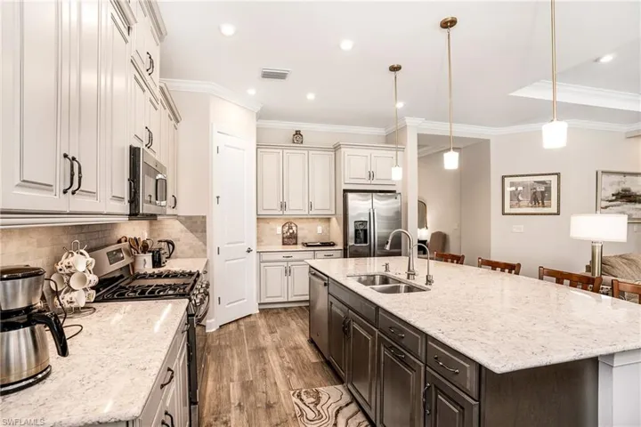 Kitchen with stainless steel appliances, light stone counters, decorative light fixtures, light wood finished floors, and a kitchen island with sink