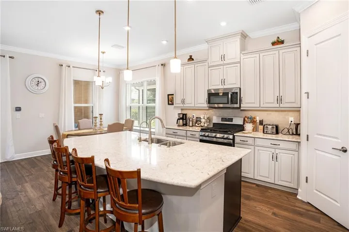 Kitchen featuring decorative backsplash, light stone counters, decorative light fixtures, stainless steel appliances, and crown molding