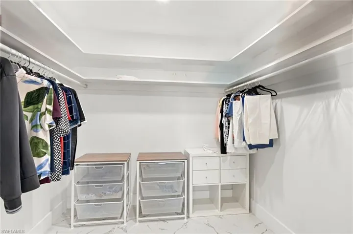 Walk-in closet featuring tray ceiling, wrap-around hanging rods, and integrated shelving with pull-out wire baskets