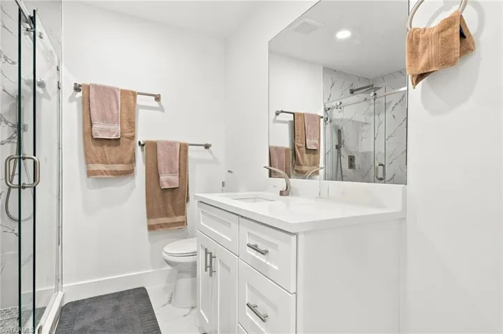 White vanity cabinet with a stone-composite countertop, undermount sink, frameless glass shower enclosure, and floor-to-ceiling tiled shower walls