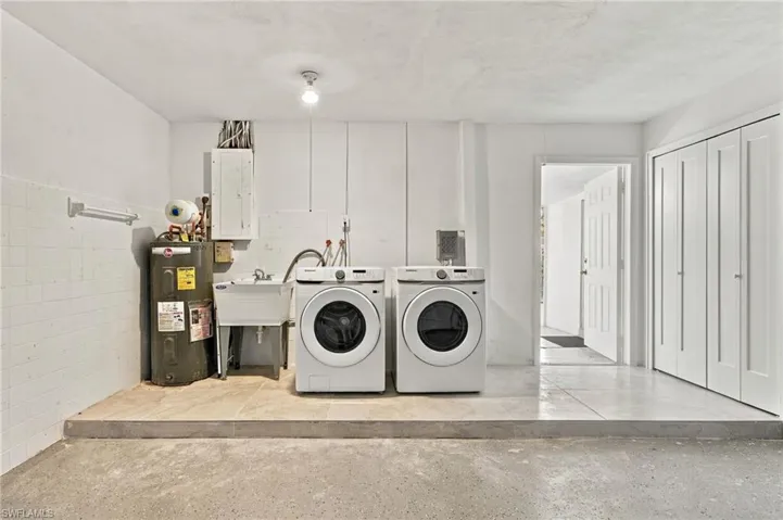 Laundry area featuring a raised tile platform, utility sink, built-in floor-to-ceiling cabinetry, and exposed concrete flooring