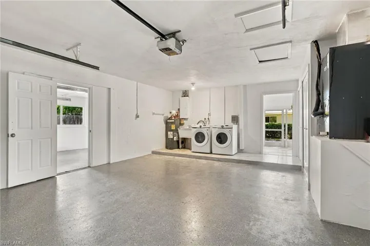 Multi-purpose garage featuring epoxy-finished flooring, a dedicated laundry area with a utility sink, and attic access points