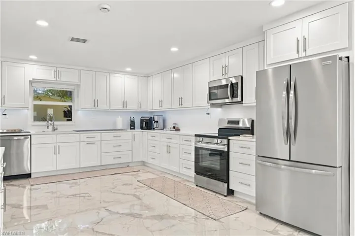 Kitchen featuring white shaker-style cabinetry, polished stone-finish flooring, stainless steel appliances, recessed ceiling lighting, and solid-surface countertops