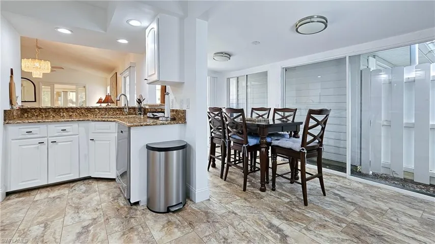 Kitchen featuring dark stone counters, white cabinets, lofted ceiling, a chandelier, and recessed lighting