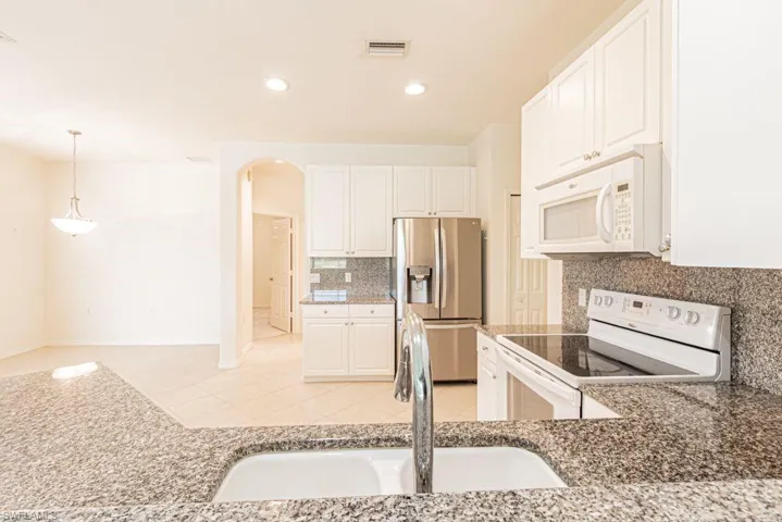 Kitchen featuring appliances, arched walkways, and white cabinetry