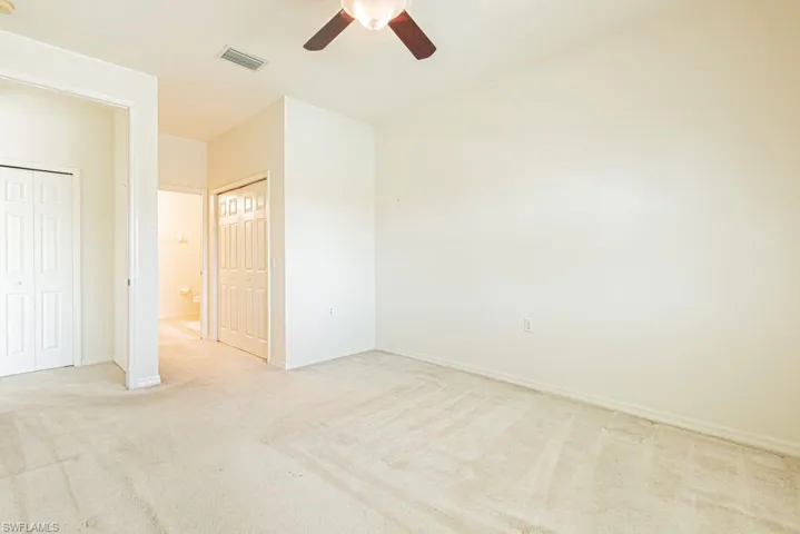 Unfurnished bedroom featuring light carpet, ceiling fan, and two closets