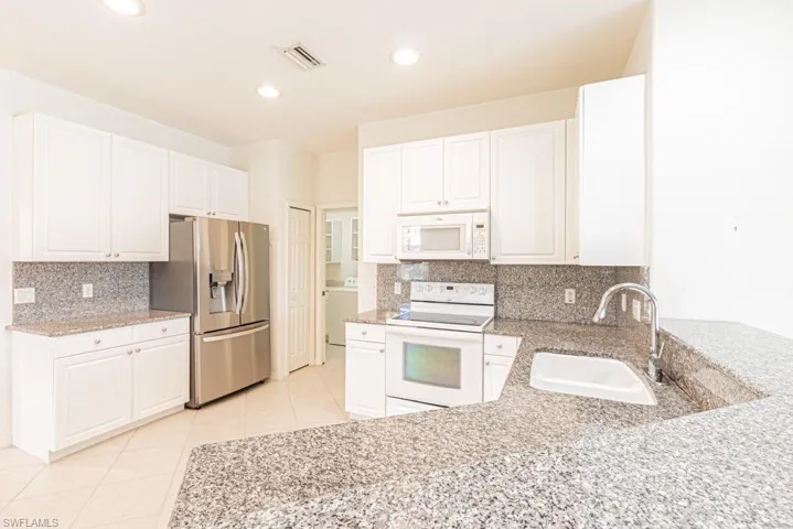 Kitchen featuring  appliances, white cabinetry, light stone counters, and recessed lighting