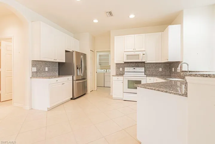 Kitchen with  appliances, dark stone countertops, independent washer and dryer, decorative backsplash, and recessed lighting