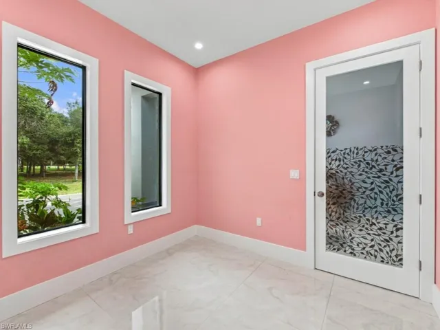 Large-format light-colored tile flooring, full-height windows with black frames, and a glass-panel door with a decorative leaf-pattern inlay