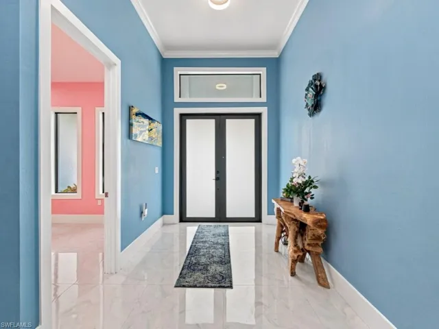 Entryway featuring double glass-paneled doors, a rectangular transom window, polished tile flooring, and crown molding