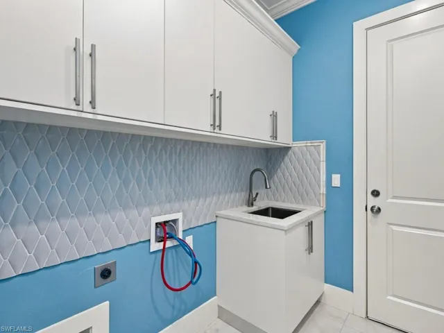 Utility space featuring white cabinetry with brushed metal pulls, a stone-surface countertop, an integrated sink with a gooseneck faucet, and diamond-patterned wall tile