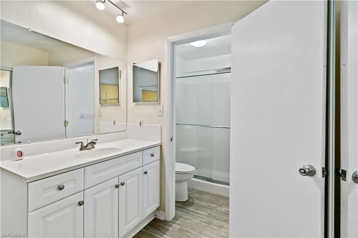 Bathroom featuring wood-type flooring, vanity, toilet, and a shower with door