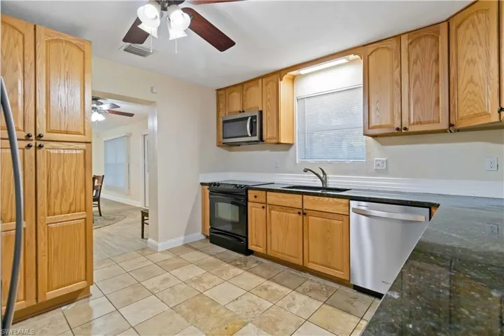 Kitchen featuring dark stone counters, ceiling fan, sink, and stainless steel appliances