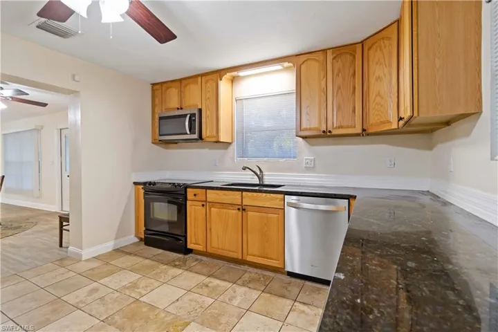 Kitchen with ceiling fan, sink, dark stone counters, and appliances with stainless steel finishes