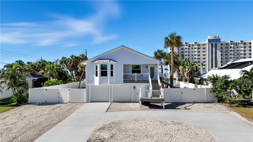 Coastal home with a gate, concrete driveway, stairs, and an attached garage - Virtually Edited Image