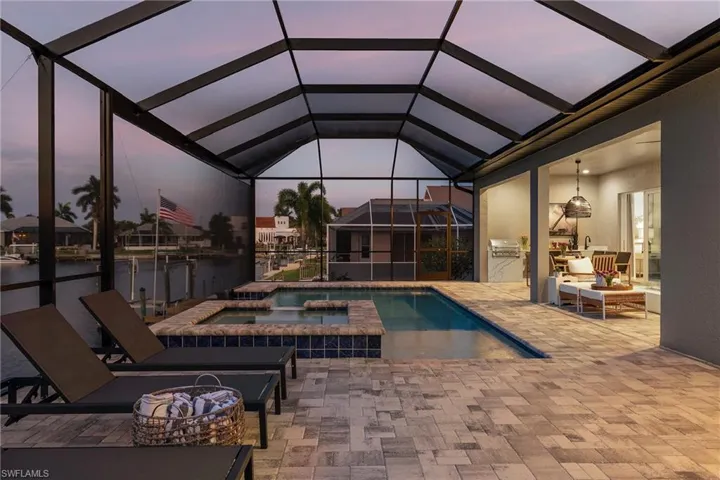 Pool at dusk with a patio area, a lanai, a pool with connected hot tub, and an outdoor kitchen