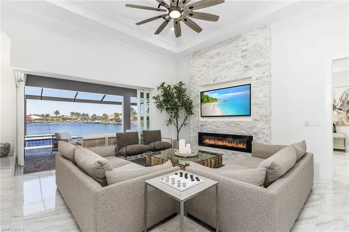 Living area with marble tiled flooring, a ceiling fan, a large fireplace, ornamental molding, and a high ceiling