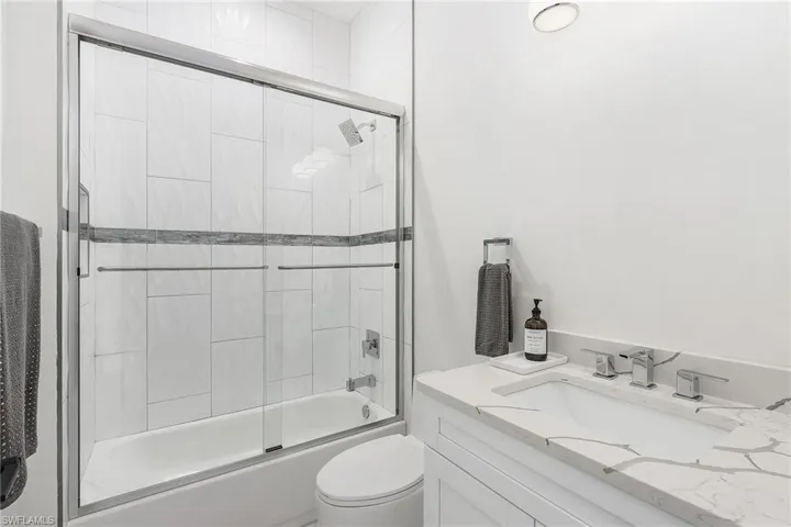 Bathroom featuring combined bath / shower with glass door, vanity, and toilet