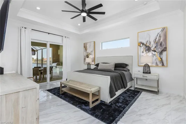 Bedroom with a tray ceiling, light marble finish flooring, ornamental molding, access to exterior, and recessed lighting