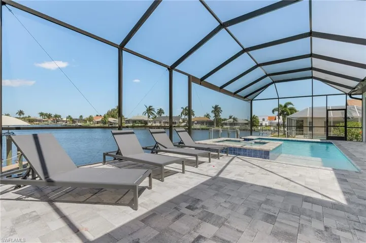 View of swimming pool featuring a patio, a pool with connected hot tub, a water view, and glass enclosure