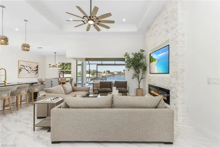 Living area with crown molding, a stone fireplace, a ceiling fan, light marble finish floors, and a chandelier