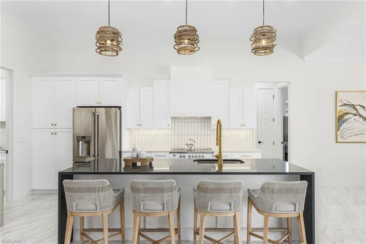 Kitchen featuring high end fridge, a sink, tasteful backsplash, a kitchen island with sink, and white cabinets