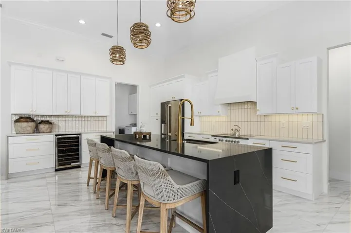 Kitchen featuring wine cooler, light marble finish floors, ornamental molding, tasteful backsplash, and a breakfast bar area