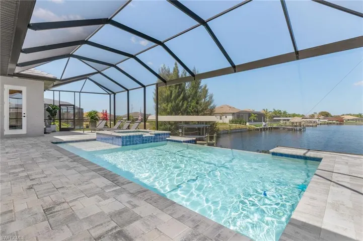 View of pool featuring a patio area, a pool with connected hot tub, a water view, and a lanai