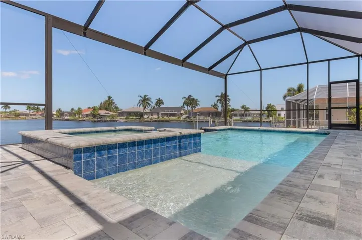 View of swimming pool featuring a pool with connected hot tub, a water view, glass enclosure, and a patio area