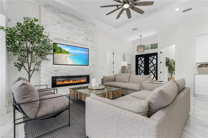 Living room with a stone fireplace, crown molding, a ceiling fan, and recessed lighting
