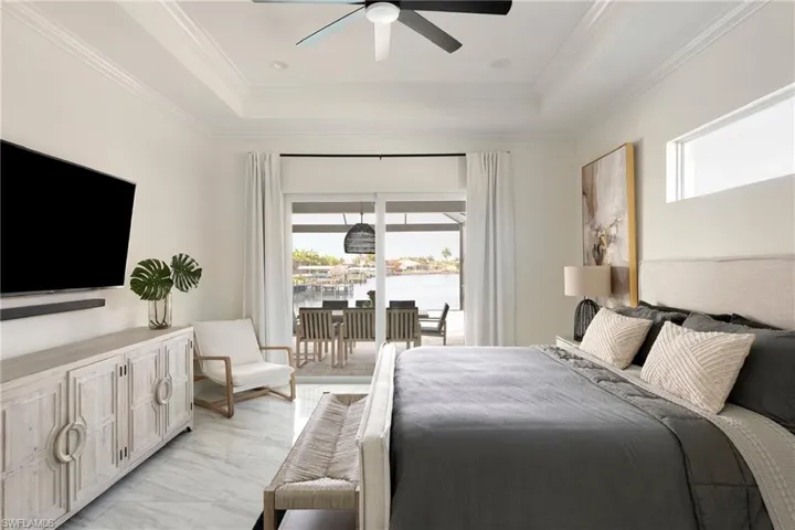 Bedroom featuring multiple windows, a raised ceiling, access to exterior, light marble finish flooring, and crown molding