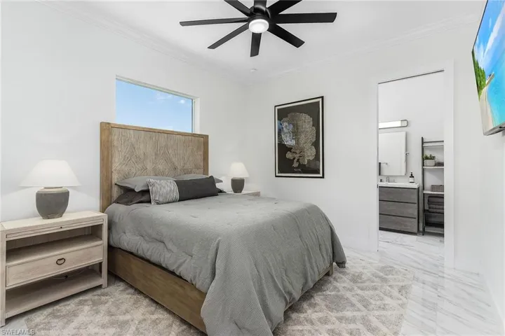Bedroom featuring ornamental molding, light marble finish floors, connected bathroom, baseboards, and a ceiling fan