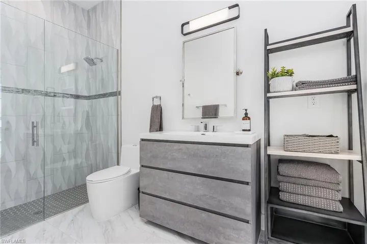 Full bath with a shower stall, vanity, marble finish floors, and toilet
